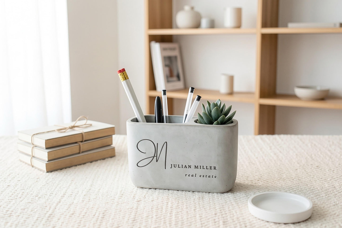 a gray container holding various office supplies, including pens, pencils, and a small succulent plant, placed on a table.