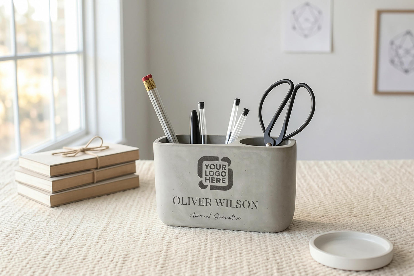 A gray pencil holder on a table, containing pens, pencils, and scissors, with a stack of books and a small white bowl nearby.