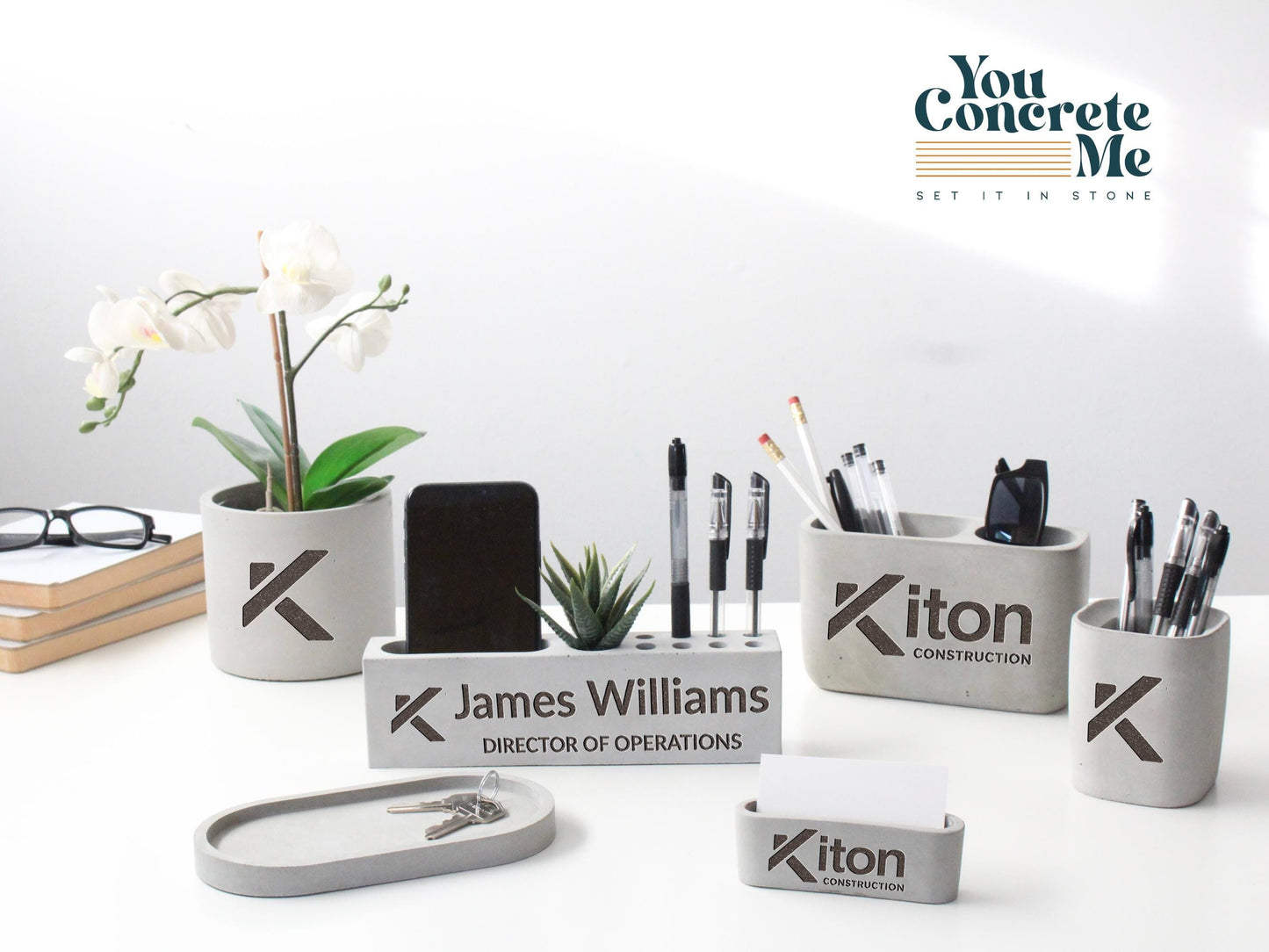 a collection of office supplies and decorative items, including a potted plant, a phone, pens, and other accessories, arranged on a white surface.